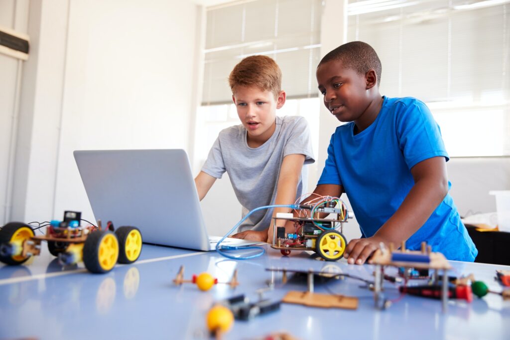 Two Male Students Building And Programing Robot Vehicle In After School Computer Coding Class